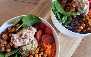 Twee witte schaaltjes met in het midden quinoa en diverse kleurrijke groenten eromheen.