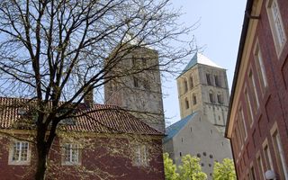 Kerkgebouw met twee hoge torens, tussen twee panden te zien.