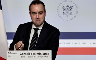 Man in donker pak staat achter een spreekgestoelte met twee microfoons.