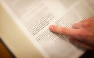 Opengeslagen Bijbel, waarbij een vinger een Bijbeltekst aanwijst.