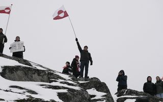 Man staat op besneeuwe rots en zwaait met een rood-witte vlag. Om hen heen staan nog wat mensen, ze steken af tegen een grijze lucht