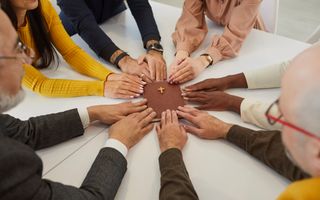 Handen van diverse jonge en oudere mensen van gemengde afkomst houden hun vingertoppen op een Bijbel. 