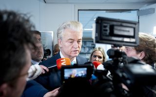 Bedrukt kijkende Wilders omringd door journalisten van radio en televisie.