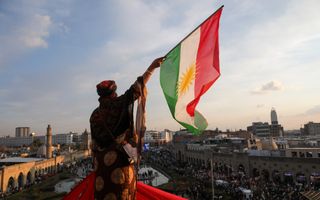 Man kijkt uit over de skyline van een stad en zwaait met een gekleurde vlag. 