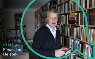 Vignet Leestips, met daarop in een grote open komma een man van middelbare leeftijd voor een boekenkast. Hij houdt een bril in zijn hand en kijkt in de camera. 
