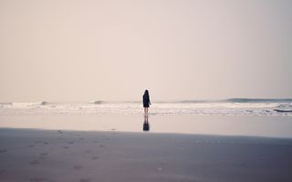 Vrouw in een zwarte jurk staat aan zee met haar voeten in de golven.