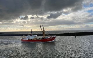 Een rode viskotter vaart tegen de avond een haven binnen. Op de achtergrond de wijde zee.