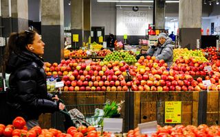Vrouw loopt met winkelwagentje langs fruitafdeling in supermarkt.
