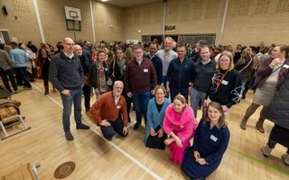 Een groep vijftigers staat lachend bij elkaar in een volle gymzaal.
