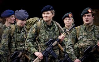 Jonge vrouw in uniform met een geweer in de hand tussen medestudenten.