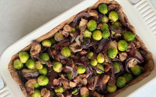 Crème ovenschaal met deegkorst met daarin spruitjes, rode ui, paddenstoelen en spekjes.