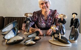 Vrouw met bril zit achter een tafel met keramieken mosselfiguurtjes die ze geboetseerd heeft.