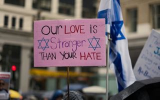 Een betoger houdt een bord vast met de tekst: Our love is stronger than your hate, met de israelische ster.