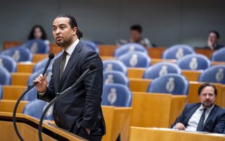 Man in pak staat bij een van de interruptiemicrofoons in de plenaire zaal van de Tweede Kamer.