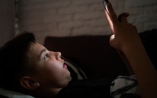 Een kind kijkt op zijn mobiel in het donker.