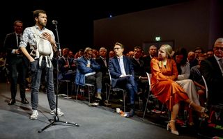 Een man met een kind in een draagzak staat achter een microfoon.