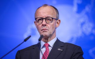 Kalende man met bril draagt donker maatpak met rode stropdas.