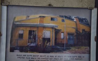Ingelijste foto van een geel huis; eronder Amhaarse tekens, en in het Engels de mededeling dat in dit huis mensen werden gemarteld, gewurgd en begraven.