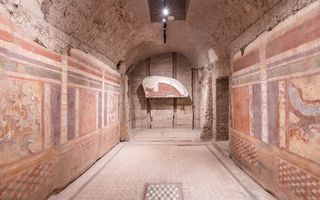 Foto van een ruimte met beschilderde stenen muren en een mozaïek op de vloer. Erboven een halfrond gewelf.