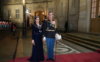 Man met donkere bril en uniform en vrouw in donkere jurk op rode loper.