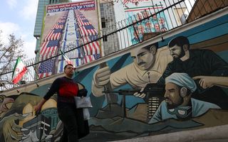 Man loopt langs muur met afbeeldingen van gewapende mannen.