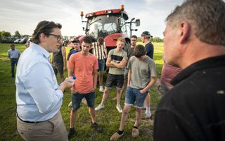 Man in gesprek met mannen en jongens die bij een rode trekker staan.