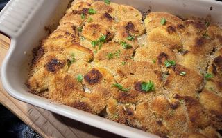 Stenen ovenschaal met gegratineerde aardappelschijfjes en wat plukjes groen.