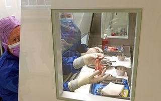 Een vrouw met twee witte handschoentjes houdt een hartklep vast, ongeveer de maat van een vinger.