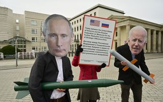 Vredesactivisten staan voor een groot gebouw. Ze dragen een tekstbord en maskers die president Poetin en president Biden voorstellen. Ze houden namaakraketten vast.