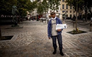 Een krantenverkoper met twee Franse kranten in zijn hand.