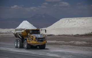 Een kiepwagen met wit lithium rijdt over een vlakte. Op de achtergrond is gebergte te zien. 