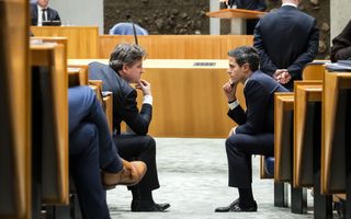 Twee mannen in pak overleggen met elkaar vanuit hun Kamerbankjes. Op de achtergrond staat CU-leider Mirjam Bikker achter het spreekgestoelte.