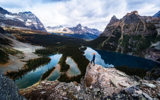 Een man staat op een rots uit te kijken over een meer. Eromheen rijzen rotsachtige bergen omhoog.