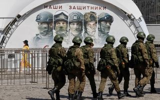 Soldaten in groene camouflagekleding lopen over een straat langs een metershoge afbeelding van militairen.