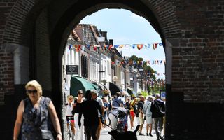 Een stenen stadspoort geeft een doorkijk in een drukke winkelstraat waarin meerdere mensen lopen.