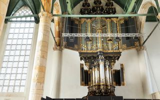 Een oud orgel hangt in een historische kerk. Het orgelfront bevat veel goudkleurige ornamenten. Aan weerszijden van de twee orgelkassen hangen groen geschilderde luiken.