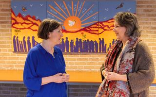 Twee vrouwen staan voor een kleurrijk kunstwerk en kijken elkaar aan.