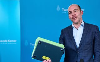 Man in pak staat met laptop en papieren in zijn hand.