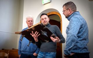 Drie mannen in een kerk, de middelste houdt een grote kanselbijbel vast.