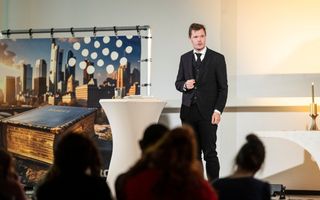 Predikant in driedelig zwart staat op een podium voor jongelui.
