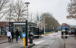 Drie mannen lopen naar een gebouwtje naast een slagboom.