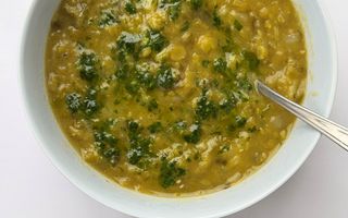 Een wit bord met daarin een geelgroene soep met een lepel erin.