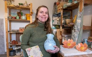 Een vrouw met een tegeltje met een gedichtje en bloemen en een keramieken vaas met tekening.