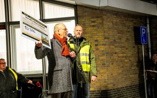 Een man met een plaquette in zijn hand op een podium voor een gebouw. 