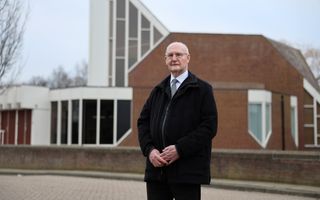 Oude man staat voor een kerkgebouw.