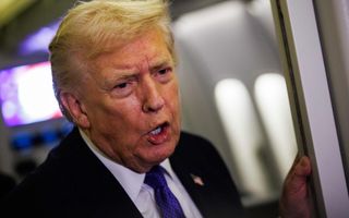 Een blonde man in maatpak staat in een deuropening.