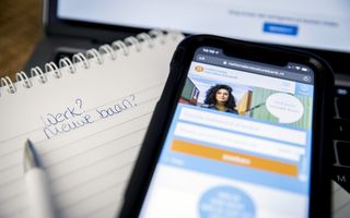 Kladblok met de tekst: Werk? Nieuwe baan? Daarnaast een smartphone met de site nationalevacaturebank.nl