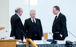 Drie mannen in zwarte pakken praten met elkaar in een kerk.