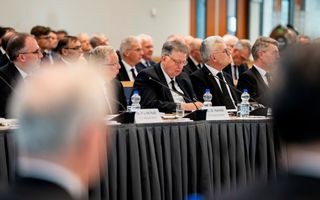 Vijf mannen in zwarte pakken zitten aan een vergadertafel.