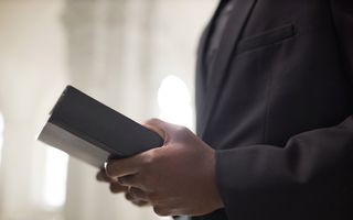 Een man –van de zijkant gezien– houdt een Bijbel in zijn handen. Hij draagt een zwart pak.